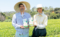 茶畑を背景に、男性と女性が横1列に並び作ったお茶を持っている写真