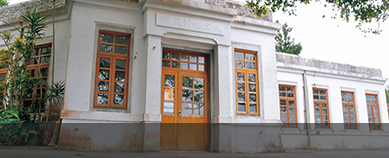 白壁に茶色の木枠の窓が付けられた建物を入口付近から撮った外観写真